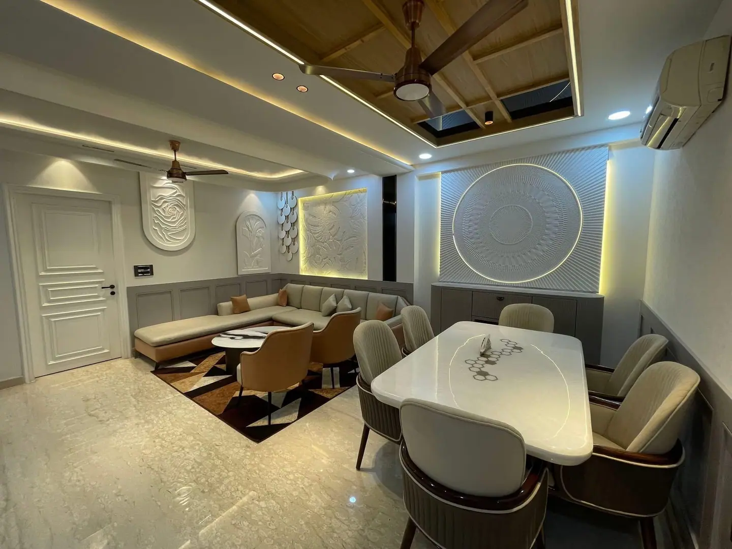 Dining area with a marble-top table and upholstered chairs beside a living space with relief wall panels and a timber ceiling